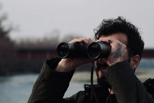 Man with a tattooed hand looking through binoculars