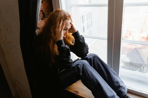 Stressed red‑haired woman sitting by window