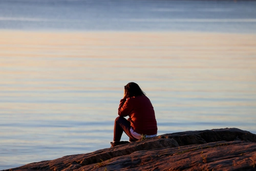 Lonely woman sitting by lakeside at sunset