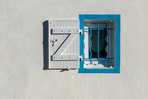 White window shutter with blue trim on plaster wall