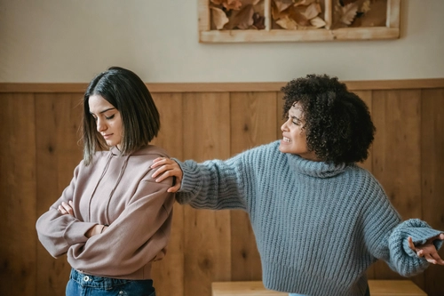 Aggrieved woman with crossed arms while another woman argues angrily beside her
