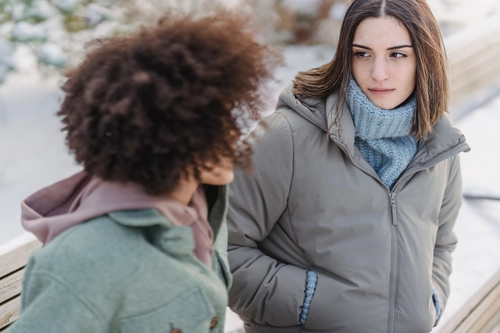 Two young women outdoors in winter, one listening silently to the other speaking