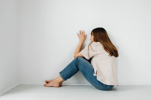 Anxious woman huddled against a wall, withdrawn posture