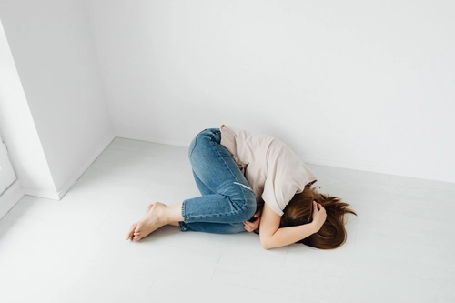 Woman curled on floor in fetal position, overwhelmed by anxiety