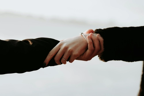 Close-up shot of two people holding hands gently outdoors