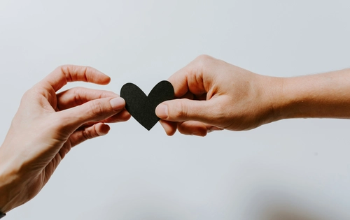 Two hands passing a black paper heart to each other
