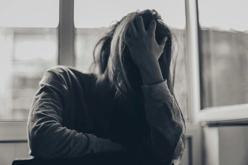 Distressed woman with head in hands, overwhelmed by emotional pain.